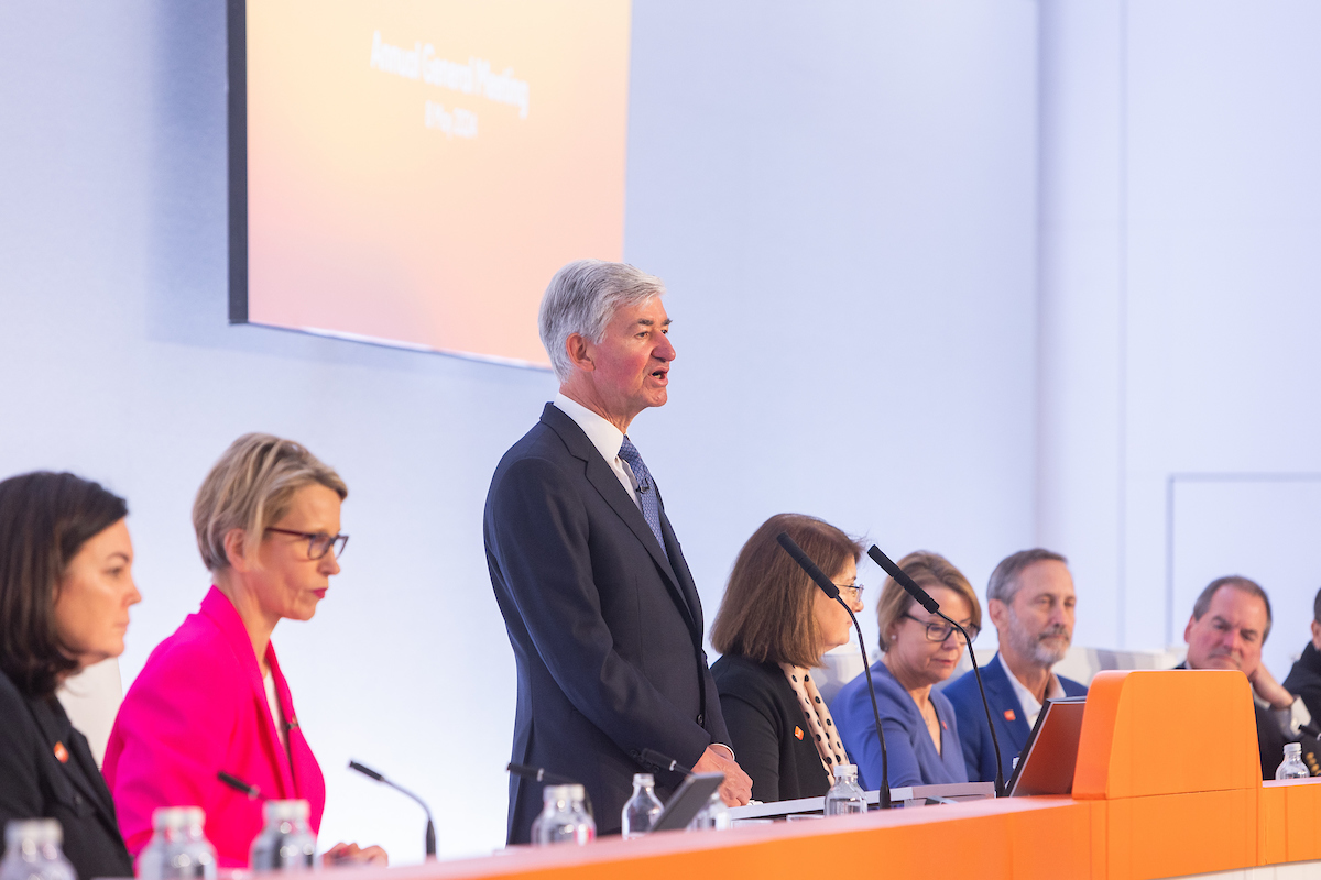 Jon Symonds, standing at podium, flanked by GSK leadership, Board Directors, all seated